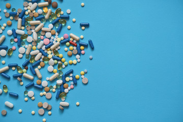 Spilled colored medications and pills on a blue background. Pharmacology and medicine struggle for health. Drug addiction. Treatment of various diseases