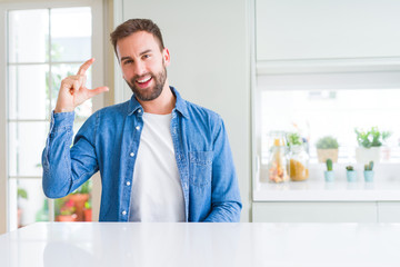 Handsome man at home smiling and confident gesturing with hand doing size sign with fingers while looking and the camera. Measure concept.