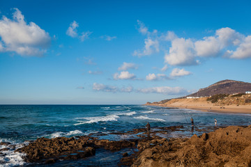 Fototapeta na wymiar Beach with fishermen and mountain in the background