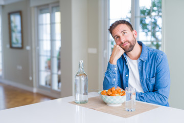 Fototapeta na wymiar Handsome man eating pasta with meatballs and tomato sauce at home with hand on chin thinking about question, pensive expression. Smiling with thoughtful face. Doubt concept.