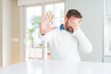 Handsome man wearing casual sweater covering eyes with hands and doing stop gesture with sad and fear expression. Embarrassed and negative concept.