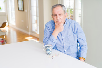 Handsome senior man drinking a cup of coffee at home thinking looking tired and bored with depression problems with crossed arms.