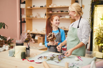 Waist up portrait of smiling mature woman creating flower compositions with teenage girl in art...