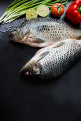 Fresh carp on a dark background with greens and vegetables.