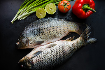 Fresh carp on a dark background with greens and vegetables.