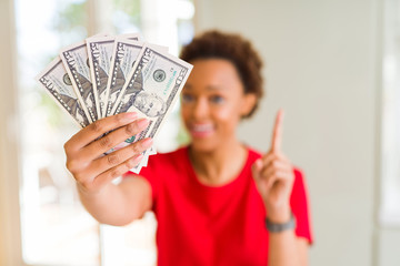 Young african american woman holding bank notes of fifty dollars surprised with an idea or question pointing finger with happy face, number one
