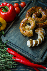 Fried sausage with herbs and spices, wooden background. Ring of baked homemade sausage. Served on a wooden board with greens and vegetables. Side view.