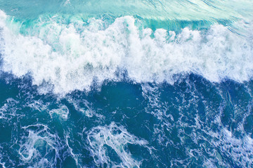 wave with white foam in the bright blue surface of the sea