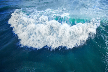 wave with white foam in the bright blue surface of the sea