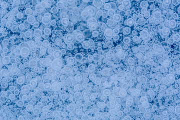 Beautiful icy background with frozen bubbles imprisoned in ice. Endless view on surface of pond or lake.