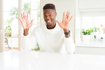 Handsome african american man on white table showing and pointing up with fingers number ten while smiling confident and happy.