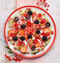Watermelon pizza, vegetarian, fruit  pizza with creamy natural yogurt and fresh fruits  on a plate, on a white wooden table, top view. Healthy and gourmet dessert or snack,  healthy eating concept