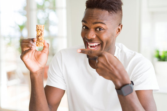 African american man eating energetic cereals bar very happy pointing with hand and finger