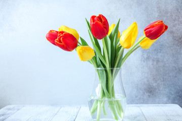 Fresh colorful tulips flowers bouquet in glass vase on wooden table In front of stone wall