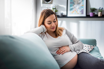 Pregnant woman relaxing on sofa at home in sunny living room