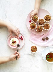 Children's hands holding a spoon and take a muffin from the plate. Muffins, cream with banana and raspberry on a light background top view