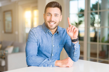 Naklejka premium Young handsome man at home surprised with an idea or question pointing finger with happy face, number one
