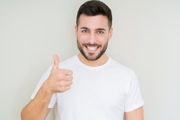 Young handsome man wearing casual white t-shirt over isolated background doing happy thumbs up...