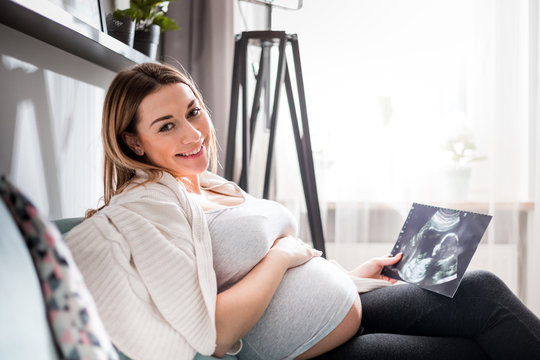Pregnant woman on sofa looking her baby on ultrasound image, usg photo