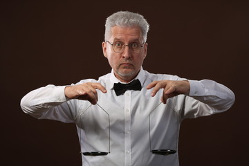 Elderly gray-haired man 50s, in white shirt, glasses and bow tie weighing something on scales with kettlebells
