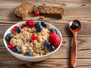 Close up view of porridge with blueberries and raspberries and grain bread on wooden background. Soft focus.