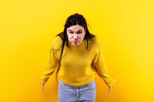 displeased girl with pouty cheeks in yellow pullover pompously looks at the camera, image on a yellow background