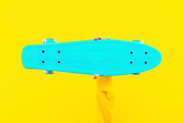 azure skateboard in hand on yellow background, concept trend and youth hobbies