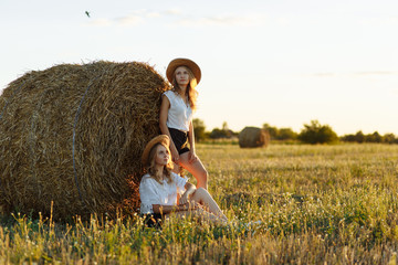 Naklejka na ściany i meble Two girls one of which is sitting near the haystack while another is standing near it