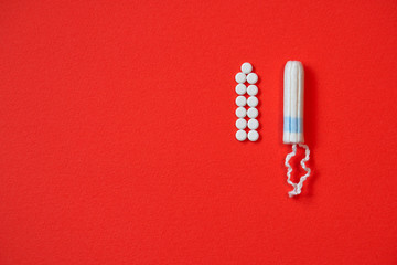 Background red on the theme of a monthly menstrual cycle. PMS and protection against it. Tampon and analgesic tablets. Intimate topic of feminine hygiene. Stock photos
