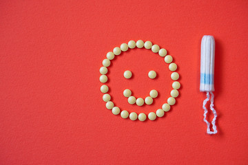Background red on the theme of a monthly menstrual cycle. Smile PMS and protection against it. Tampon and analgesic tablets. Intimate topic of feminine hygiene. Stock photos