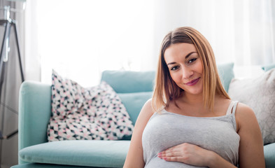 Beautiful smiling pregnant woman sitting on floor at home, looking at camera