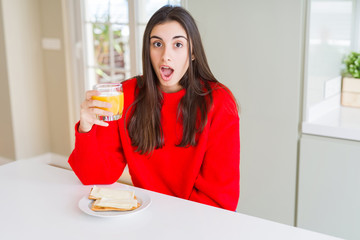 Beautiful young woman eating toasts and orange juice for snack or breakfast scared in shock with a surprise face, afraid and excited with fear expression