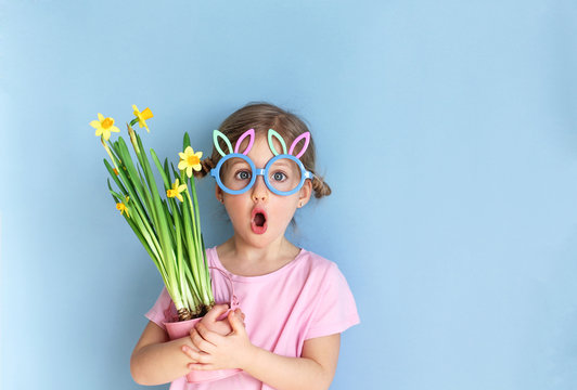 Cute little child wearing bunny ears glasses and holding flowers on Easter day. Easter girl portrait, funny emotions, surprise. Copyspace for text