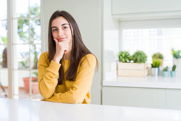 Fototapeta premium Beautiful young woman wearing yellow sweater looking confident at the camera with smile with crossed arms and hand raised on chin. Thinking positive.