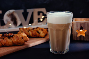 Coffee with milk froth. Next to a delicious dessert with chocolate. In the background, garland lights in blur.