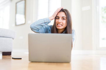 Fototapeta premium Beautiful young woman laying on the floor using laptop stressed with hand on head, shocked with shame and surprise face, angry and frustrated. Fear and upset for mistake.