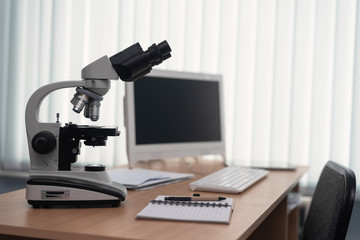 Microscope and a computer on a table in a laboratory on a window light background.