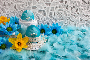 Wielkanocna kompozycja z niebieskimi pisankami, żółtymi i niebieskimi kwiatami oraz piórami na tle białej koronki © Monika
