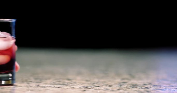 Close up of hand grabbing a mixed cocktail off of bar in slow motion