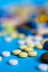 Spilled colored medications and pills on a blue background. Pharmacology and medicine struggle for health. Drug addiction. Treatment of various diseases