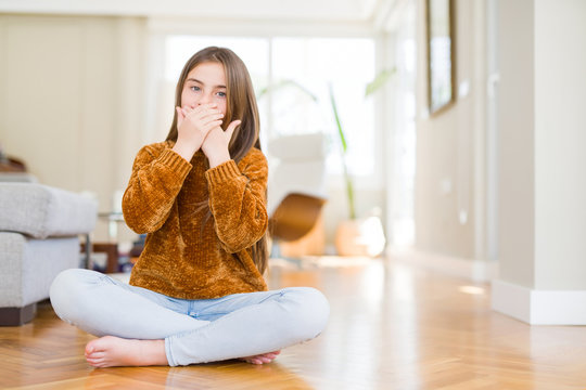 Beautiful young girl kid sitting on the floor at home shocked covering mouth with hands for mistake. Secret concept.
