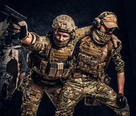 Combat conflict, special mission. The military soldier carrying teammate out of the battlefield. Studio photo against a dark textured wall