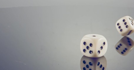 Slow motion macro shot of white dice falling and rolling on reflective surface