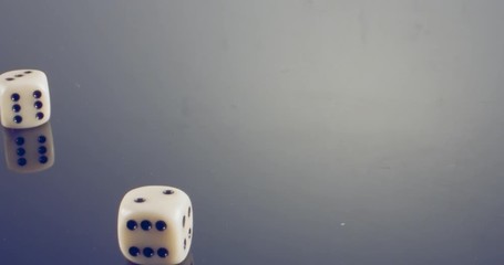 Slow motion macro shot of white dice falling and rolling on reflective surface