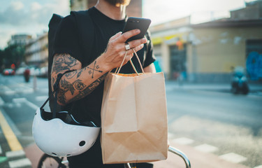 Courier bicycle delivery food service at home. Tattooed Man courier using a map app on mobile phone to find the delivery address in the city.