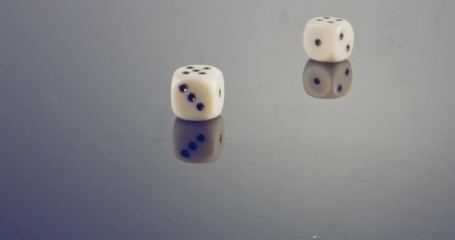 Slow motion macro shot of white dice falling and rolling on reflective surface