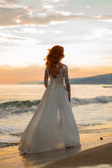 Fototapeta na wymiar The red-haired bride. Wedding. Sea. Sandy beach. Sunset.