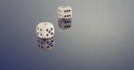 Slow motion macro shot of white dice falling and rolling on reflective surface