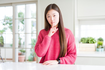 Fototapeta na wymiar Beautiful Asian woman wearing pink sweater on white table asking to be quiet with finger on lips. Silence and secret concept.