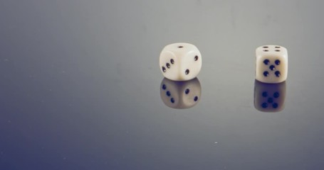 Slow motion macro shot of white dice falling and rolling on reflective surface